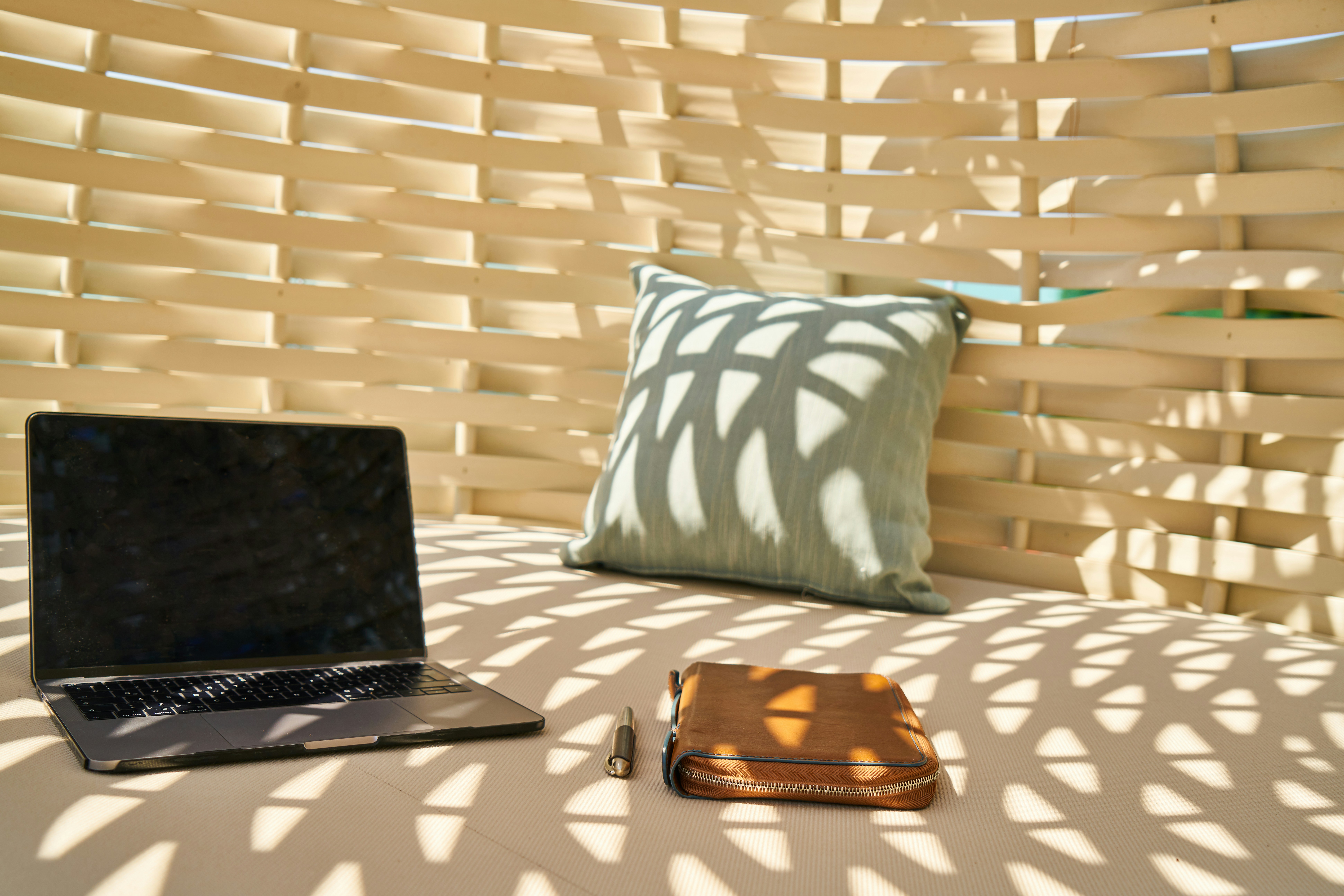 Laptop und Notizbuch auf einer hellen Liegefläche im Schatten eines geflochtenen Sonnendachs — Umgebung für eine Online-Beratung
